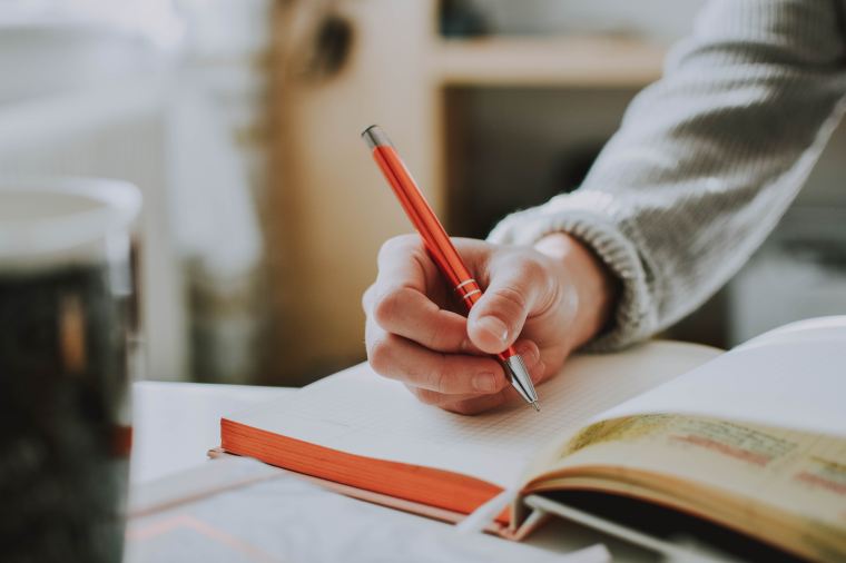 student holding pen over open book at a table